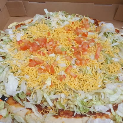 Taco pizza with lettuce, tomato, and cheddar